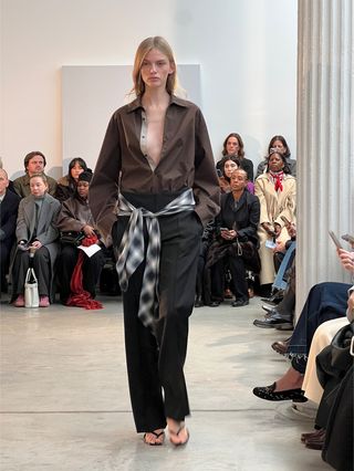 A brown shirt, plaid waistband, and black trousers from the F/W 25 Kallmeyer runway collection.