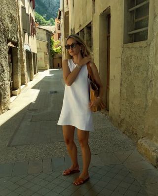 Anouk Yve wearing a white minidress, tote bag, and brown Hermès Oran sandals.