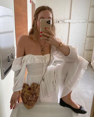 Laura Sanderson wearing a white off-the-shoulder dress with a crossbody bag and ballet flats.